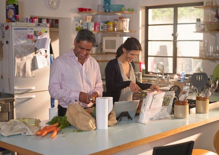 Casal cozinhando juntos na cozinha de casa consultando receita