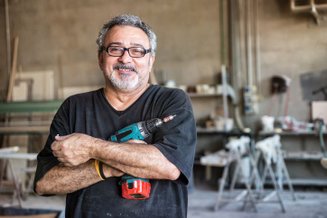 Homem em oficina segurando uma furadeira de impacto, usando uniforme de trabalho, com se sentindo confiante na marcenaria.