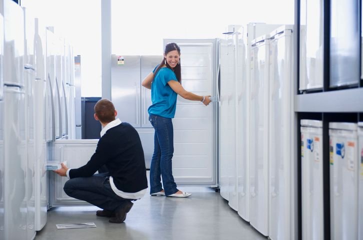 Imagem de uma loja de eletrodom&eacute;sticos mostrando uma mulher e um homem pensando se geladeira inverter vale a pena.