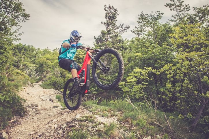 Ciclista fazendo salto em trilha de mountain bike, mostrando pneu Maxxis com cravos para uso off-road em terreno seco e acidentado.
