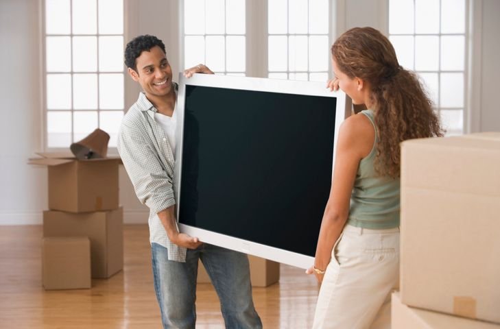 casal fazendo mudan&ccedil;a e carregando uma TV Android 32 polegadas em uma sala cheia de caixas 