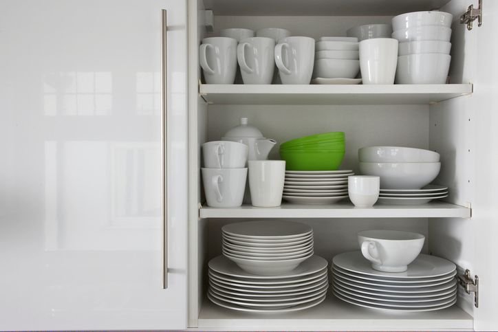 Arm&aacute;rio a&eacute;reo de cozinha com diversas lou&ccedil;as brancas incluindo pratos, x&iacute;caras, bowls e uma pe&ccedil;a verde, organizado e otimizado pra espa&ccedil;o.