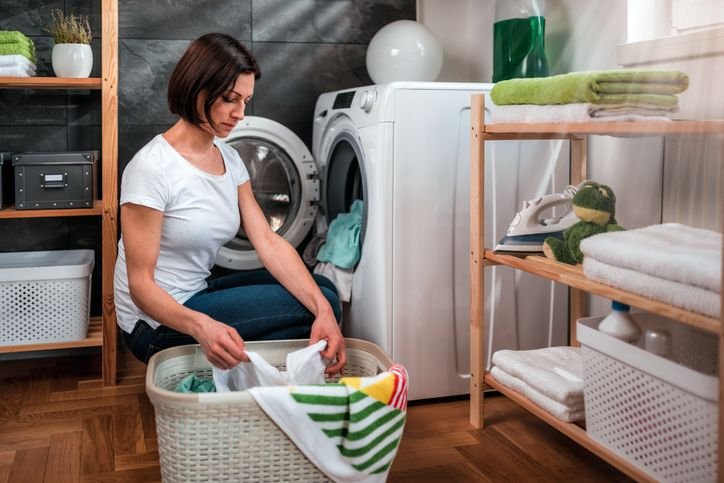 Lavanderia doméstica com máquina lava e seca 15kg aberta e uma mulher pegando roupas coloridas, ambiente de limpeza em casa.