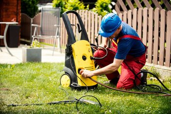 Homem realizando manutenção e verificando conexões de uma lavadora de alta pressão em jardim residencial, ajustando mangueira e equipamento pra uso seguro