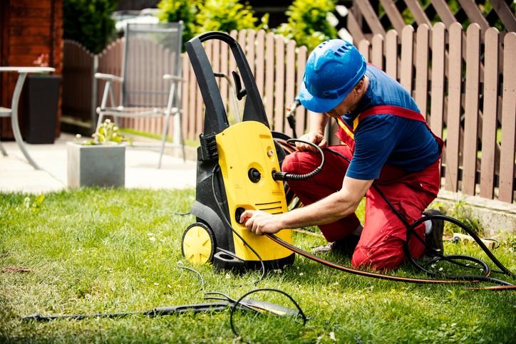 Homem realizando manutenção e verificando conexões de uma lavadora de alta pressão em jardim residencial, ajustando mangueira e equipamento pra uso seguro