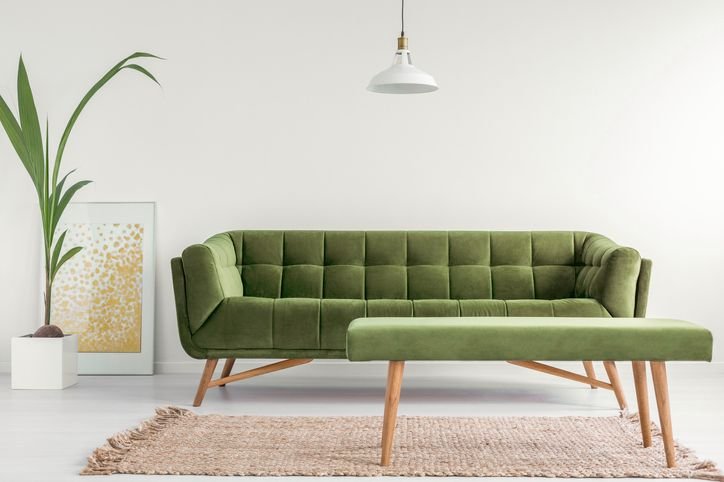 Sof&aacute; verde claro na decora&ccedil;&atilde;o moderna de sala de estar, acompanhada de uma planta ornamental e uma lumin&aacute;ria, criando um ambiente acolhedor e elegante.
