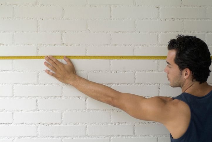 Pessoa com trena medindo parede em casa.