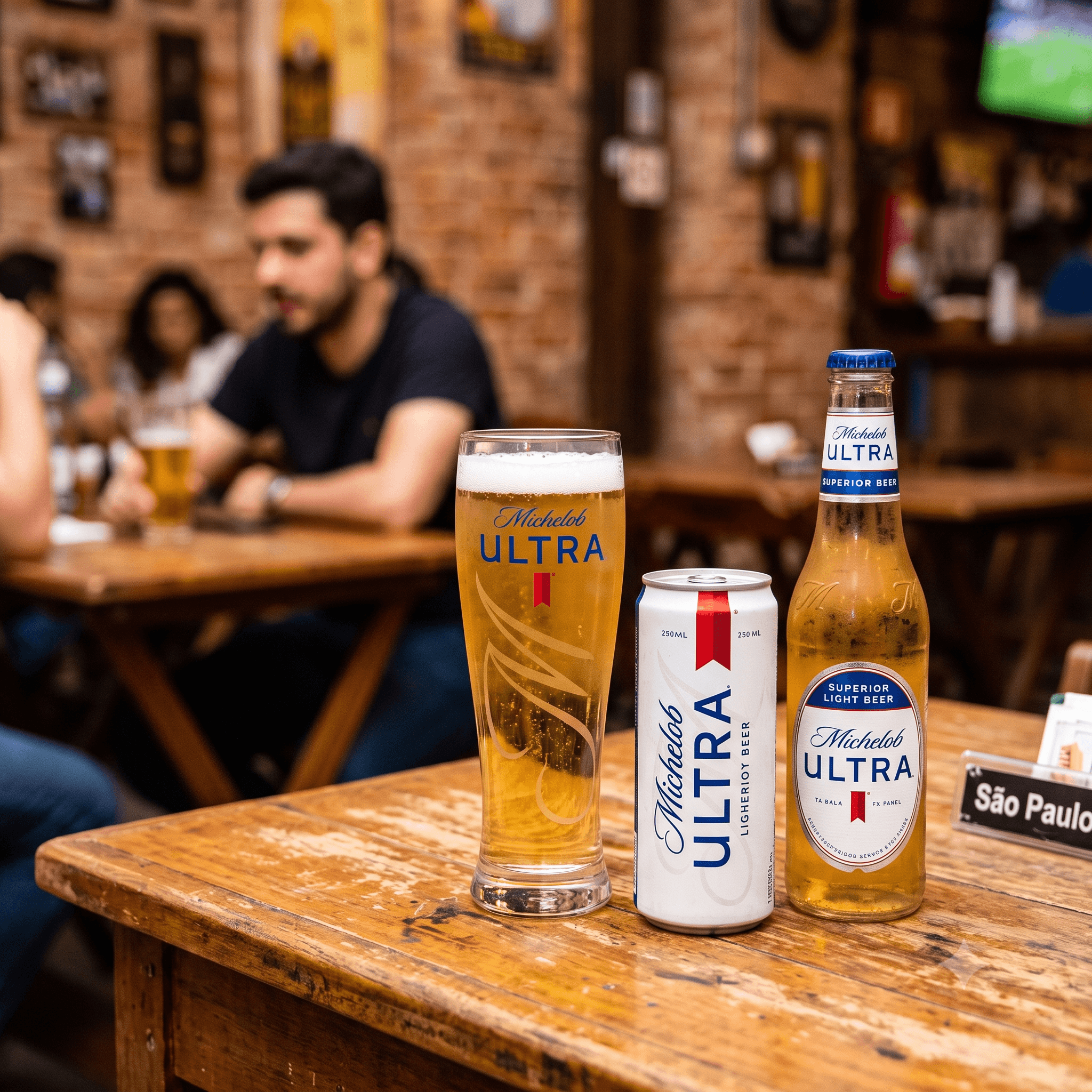 Copo com cerveja Michelob sobre uma mesa de bar, com pessoa ao fundo desfocada, sugerindo degustação de cerveja em ambiente informal.