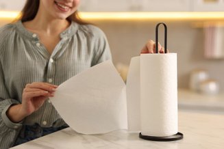 Mulher segurando folhas de papel toalha sobre bancada de cozinha