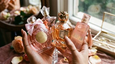 Mãos femininas segurando frascos de perfume importado feminino doce em close-up, destacando diferentes fragrâncias