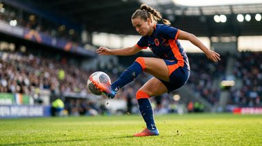 Jogadora com chuteira de grana dominando a bola, fotografada de baixo para cima.